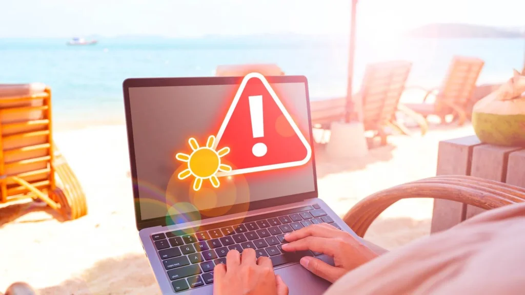 A laptop on a sunny beach displays a red warning symbol with a sun icon, indicating an overheating problem.